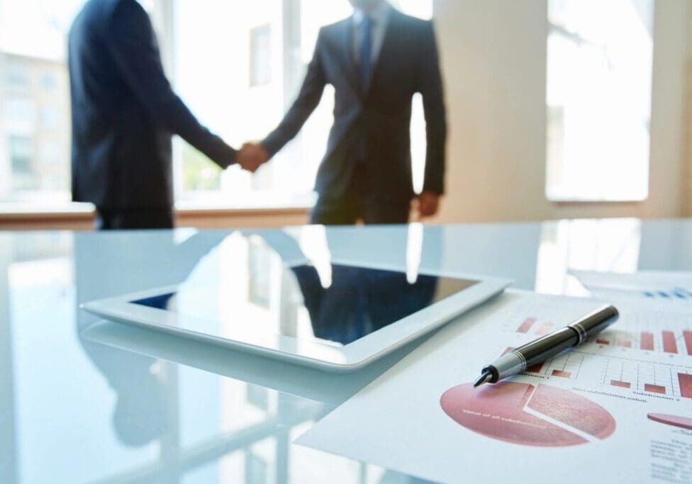 Two men shaking hands over a tablet.